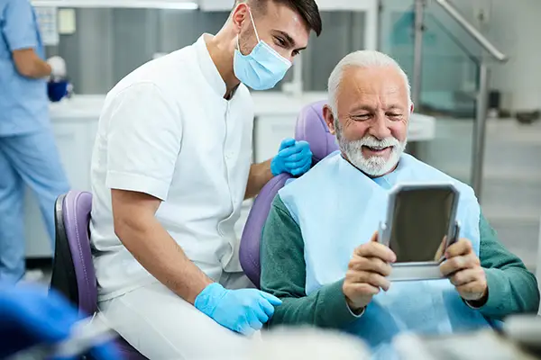 Happy, senior patient looking at his restored smile in a mirror at San Francisco Dental Arts in San Francisco, CA