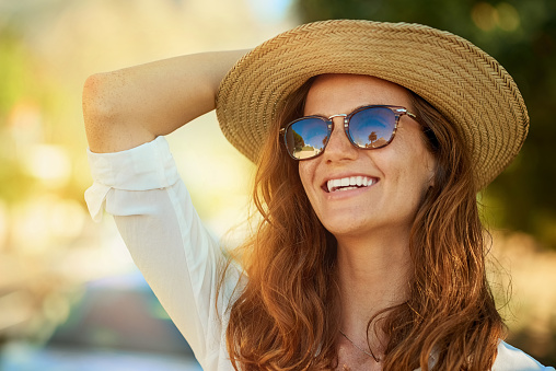 Woman with long red hair wearing sun glasses and a sun hat.