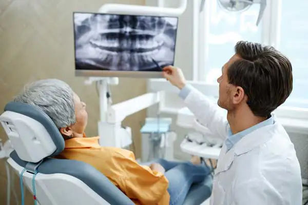 Back view of male dentist pointing at tooth X-ray image on screen during dental implant consultation at San Francisco Dental Arts in San Francisco, CA Back view of male dentist pointing at tooth X-ray image on screen during dental implant consultation at San Francisco Dental Arts in San Francisco, CA