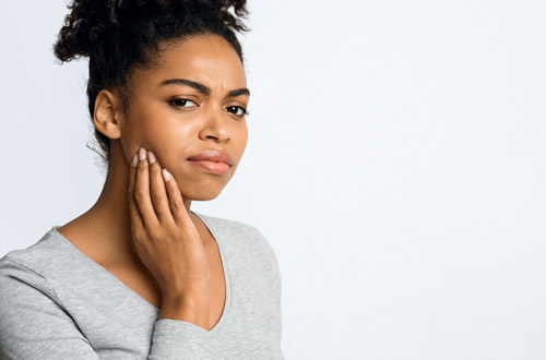 Woman touches her cheek, where there could be a potential cavity.