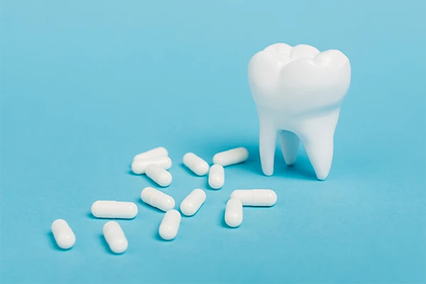 3D-printed tooth sitting on a blue background next a scattered number of plain, white pills