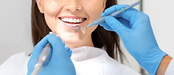 Close-up of a woman smiling as a dentist uses a mirror and scaler for a dental examination.